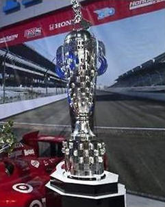 L'angolo acuto di Lino Manocchia - INDIANAPOLIS, 20.5.2013  Compiamo un salto arretrato trentennale onde dare uno sguardo alla 500 miglia di Indianapolis, laFata Morgana dei piloti di mezzo mondo, venuti per la classica gara del Memorial Day, la corsa piu eccitante del globo, sfidando la fortuna, il pericolo ed anche una triste fama, in quanto molti piloti son caduti sulla pista stregata della Indiana. Nella foto il prestigioso trofeo dove sono incisi tutti i volti e i nomi dei vincitori a Indianapolis.